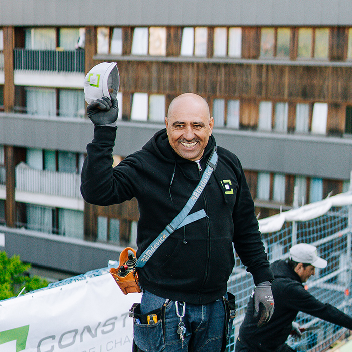 Vous souhaitez évoluer et grandir dans un environnement de travail sain, agréable et évolutif ? Ouvrier souriant qui salue l'objectif en tirant son casque de chantier