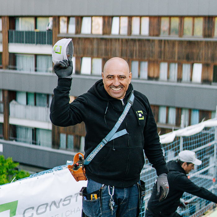 Ouvrier souriant qui salue l'objectif en tirant son casque de chantier