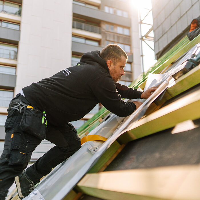 Toiture inclinée ouvrier construbel de profil qui travaille sur un toit de bâtiment public en ville