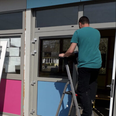 Un installateur de châssis en PVC dans une cours de récréation d'une école