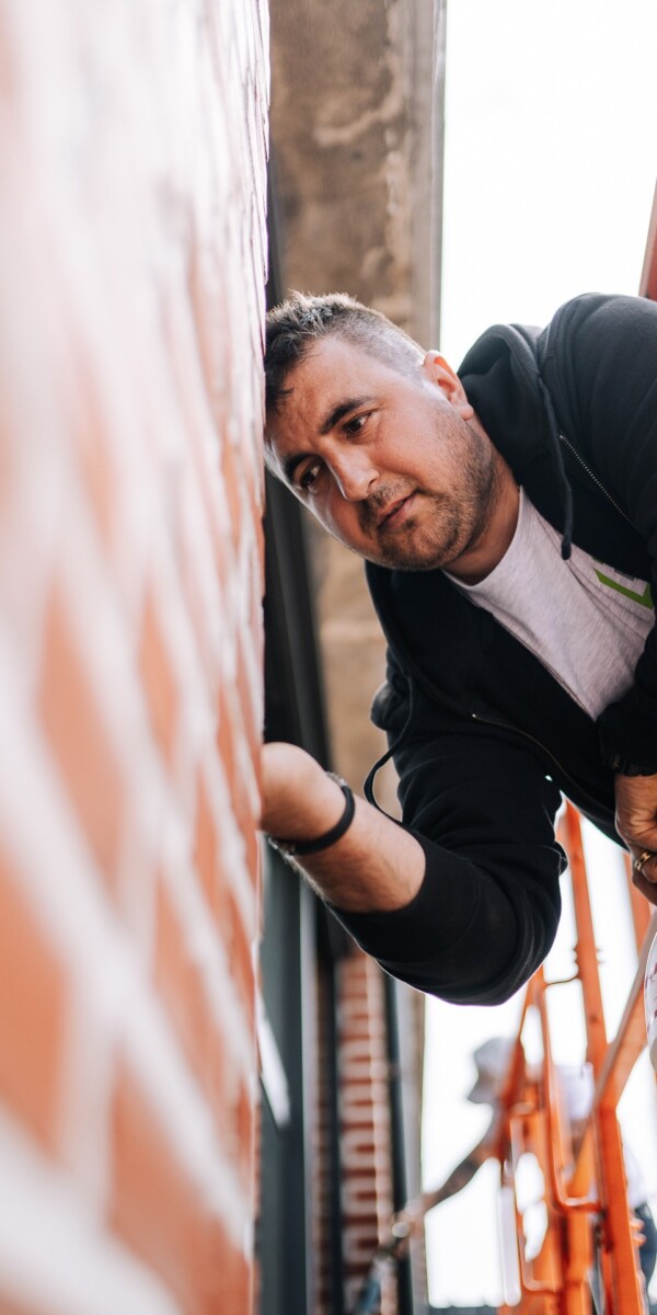 Ouvrier à l'extérieur sur une nacelle et penché vers la façade d'un bâtiment industriel pour installer un châssis en PVC